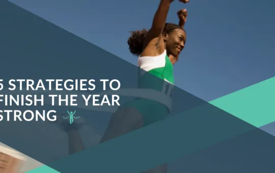 CutTime Blog Article 5 Strategies for Finishing the Year Strong with a black woman runner smiling with hands raised as she crosses the finish line.